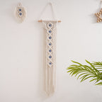 Handwoven cotton rope evil eye wall hanging tapestry with tassels on beech wood rod, ideal for bedrooms, living rooms, or homestays.