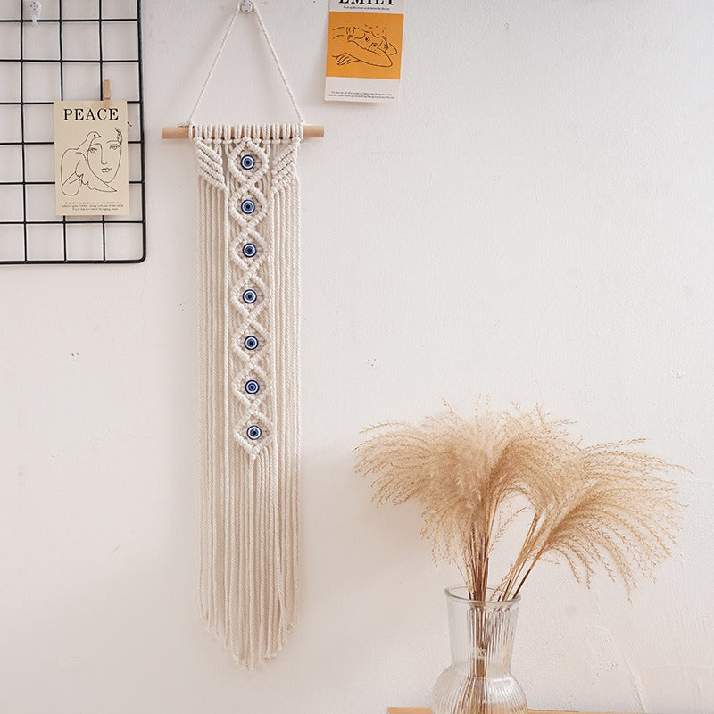 Handwoven cotton rope evil eye wall hanging tapestry with tassels and beech wood rod, perfect for boho bedroom or living room décor.