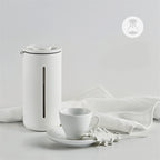 Portable Borosilicate glass French press with white and black frame, ideal for coffee and tea at home, office, or travel.